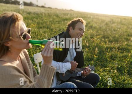 Ora legale. Bella giovane coppia godendo del tempo in campo intorno all'erba. Stile di vita, amore, datazione, concetto di vacanza. Privato. Donna che beve birra, uomo Foto Stock