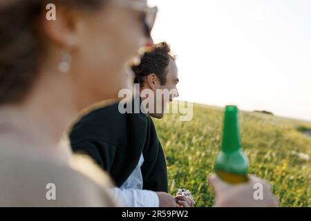 Ora legale. Bella giovane coppia godendo del tempo in campo intorno all'erba. Stile di vita, amore, datazione, concetto di vacanza. Privato. Donna che beve birra, uomo Foto Stock