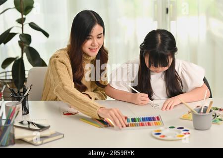 Piccola ragazza asiatica concentrata disegno con la madre in soggiorno. Concetto di svago della casa della famiglia Foto Stock