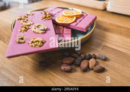 Barrette di cioccolato bianco e rosso rubino con fette di arancia e semi di cacao su un tavolo. Foto di alta qualità Foto Stock