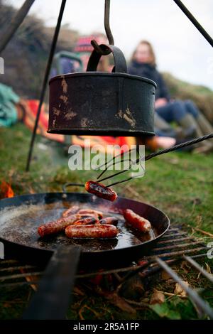 Una famiglia grigliate salsicce e bolle d'acqua su un fuoco da campo vicino Ellingstring, North Yorkshire, Inghilterra, Regno Unito, il 22 2009 marzo. Foto Stock