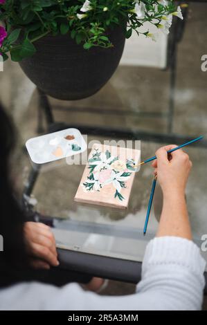 Close up of woman creatively painting flowers on canvas outdoors Foto Stock