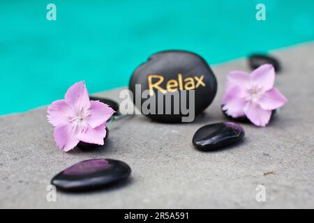 Massaggiare in pietra con la parola RELAX e fiori rosa Foto Stock