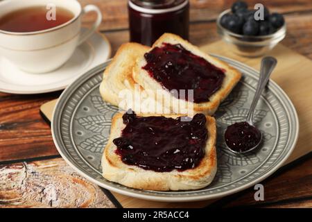 Toast deliziosi con marmellata di mirtilli e una tazza di tè su un tavolo di legno Foto Stock
