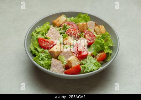 Insalata di verdure con pollo e formaggio su un tavolo grigio. Caesar insalata in un piatto grigio. Foto Stock