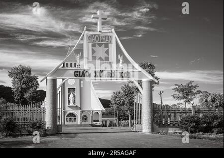 Il cancello d'ingresso per la chiesa parrocchiale cattolica di Ro Koi nel distretto di SA Thay, Provincia di Kontum, Vietnam. La chiesa rosa e gialla era ufficialmente aperta Foto Stock