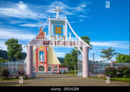 Il cancello d'ingresso per la chiesa parrocchiale cattolica di Ro Koi nel distretto di SA Thay, Provincia di Kontum, Vietnam. La chiesa rosa e gialla era ufficialmente aperta Foto Stock