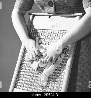 Facendo la lavanderia nel 1960s. Una signora sta usando un lavabo per pulire la lavanderia sporca. L'utensile è stato progettato per lavare a mano gli indumenti strofinandoli contro la serie di creste di ondulazioni. Questo fatto ripetutamente ha fatto pulire i vestiti. Il lavabo è diventato più conosciuto per il suo uso secondario come strumento musicale. Svezia 1963. Kristoffersson rif CX76-11 Foto Stock