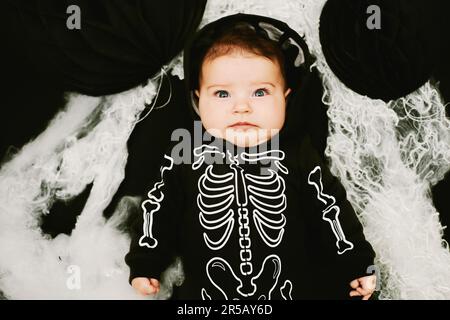 Ritratto di Halloween di adorabile bambino indossando costume scheletro, posando su sfondo nero ricoperto di ragnatela Foto Stock