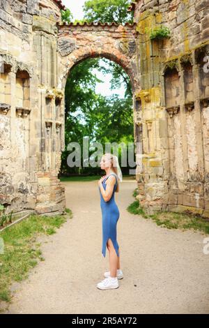 ragazza meditando nelle rovine di una vecchia chiesa e mettere le mani su un cuore Foto Stock