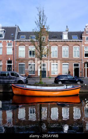 Haarlem, Paesi Bassi - Aprile 12. 2022: Barca arancione brillante ormeggiata sul fiume Sparne in primavera. Riflessi nell'acqua. Foto Stock