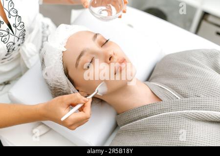 Il cosmetologo pulisce il volto di una bella donna caucasica con un gel speciale prima di applicare una maschera, peeling, scrub. Procedure per la cura della pelle del viso in un salone di bellezza Foto Stock