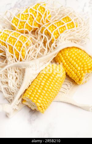 Cinque pezzi di mais in un sacchetto in maglia di cotone su un banco da cucina in marmo bianco in una vista dall'alto Foto Stock