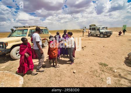 30th dicembre 2017, Parco Nazionale di Serengeti, Tanzania-A Tourist condivide i suoi spuntini e aiuta i bambini Maasai con acqua e denaro Foto Stock