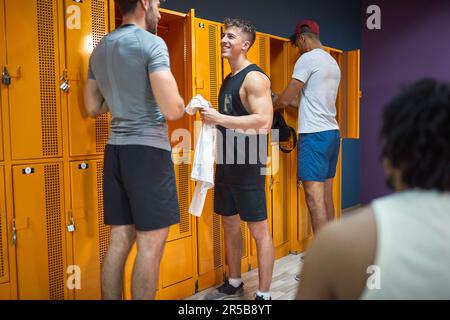 Colpo di corpo completo di giovani uomini in abbigliamento sportivo nella spogliatoio parlare e prepararsi per la sessione di allenamento in palestra. Salute, benessere, stile di vita Foto Stock