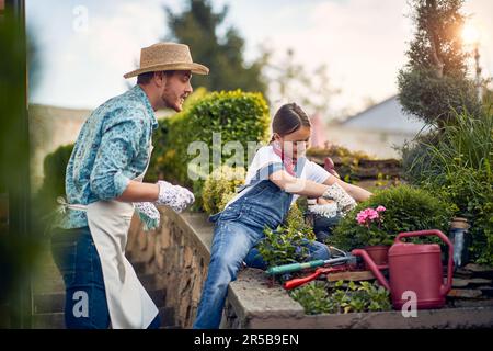 Legame tra padre e figlia mentre lavorano fianco a fianco nel loro giardino. La ragazza è arrossed nei suoi compiti di giardinaggio, mentre suo padre è in piedi ne Foto Stock