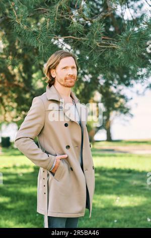 Ritratto all'aperto di bel giovane uomo con capelli rossi, vestito di beige Foto Stock