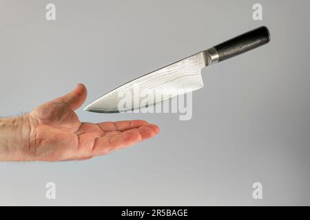 il coltello da cucina affilato cade con la lama sulla mano maschio. Prevenzione degli incidenti Foto Stock