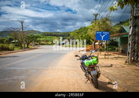 Una grande motocicletta parcheggiata vicino a un cartello stradale blu sulla strada QL40 che punta ai confini della Cambogia e del Laos in Bo Y comune, Ngoc Hoi distretto, nel cent Foto Stock