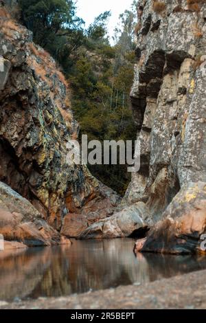 Un fiume tranquillo si snoda attraverso un paesaggio rustico di grandi massi, alberi e vegetazione lussureggiante Foto Stock