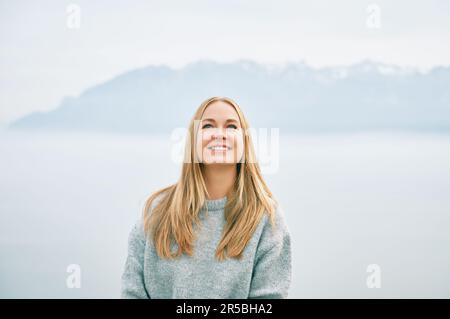Ritratto all'aperto di felice bella giovane donna che si rilassa in montagna sopra le nuvole, indossando un pullover grigio Foto Stock