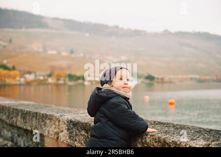 Ritratto all'aperto di adorabile bambina che gioca sul lago in una fredda giornata autunnale, indossando giacca e cappello caldi Foto Stock