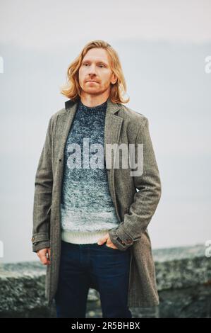 Ritratto all'aperto di un giovane uomo dai capelli rossi, con indosso un pullover e un cappotto, giorno di nebbia fredda Foto Stock
