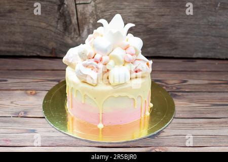 Dolce di compleanno rosa con cioccolato bianco fuso, corona fondente, meringhe e marshmallow su sfondo rustico Foto Stock