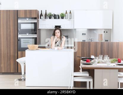 Orgogliosa e felice, una giovane donna con trecce e un abito floreale mostra la sua nuova cucina. Lo spazioso e lussuoso design europeo eleva la sua q Foto Stock