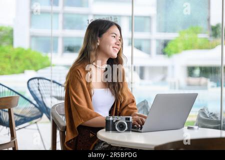 Donna asiatica che utilizza una fotocamera digitale e un computer portatile al bar Foto Stock