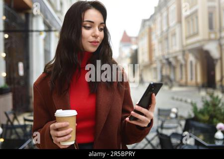 Donna d'affari usa il telefono cellulare all'esterno tenendo una tazza di caffè. Foto Stock
