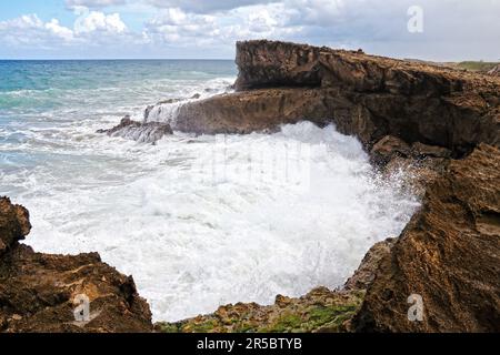 Una maestosa grotta oceanica con una grande formazione rocciosa e un flusso d'acqua che esce dal suo ingresso Foto Stock