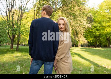 Moglie e marito camminano a Park. La donna appoggia la testa alla spalla dell'uomo. Relazione, Unione. Godersi il tempo insieme. Donna guarda la fotocamera, retro Foto Stock