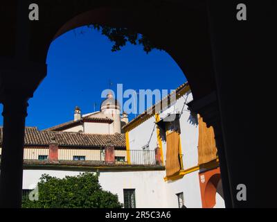 Un uomo maturo è seduto in una tranquilla contemplazione in una giornata di sole nel cortile protetto di un edificio storico, incorniciato da un arco di pietra ornato Foto Stock