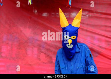 Una figura maschile si vede in piedi sotto un tarp rosso brillante mentre indossa una maschera blu Foto Stock