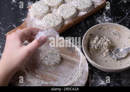 foto fare un dessert di ricotta con semi di papavero, cheesecake su un asse di legno e la mano nella farina Foto Stock