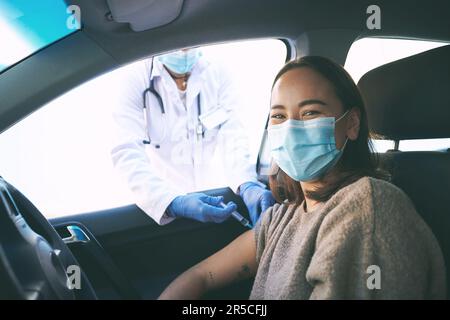 Aghi non spaventare me, ammalarsi fa. Una giovane donna mascherata che riceve un'iniezione in un drive Covid-19 attraverso il centro di test. Foto Stock