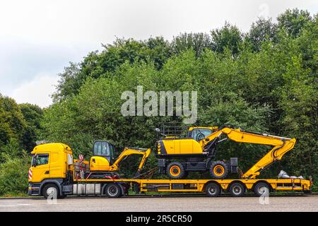 Rimorchio con caricatore basso che trasporta due escavatori parcheggiando in un'area di parcheggio pubblica di un'area di sosta per autocarri. Foto Stock