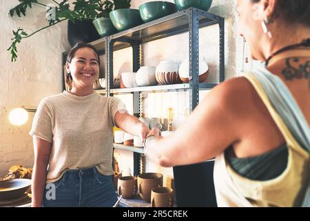 Benvenuto nella community di Crafting. due giovani donne che scuotono le mani in uno studio di ceramica. Foto Stock