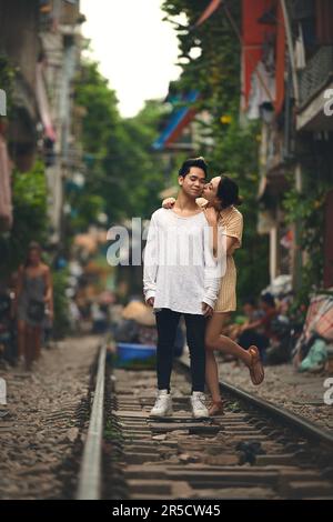 I suoi baci fanno sorridere il mio cuore. Una giovane coppia che condivide un momento romantico sulle piste dei treni per le strade del Vietnam. Foto Stock