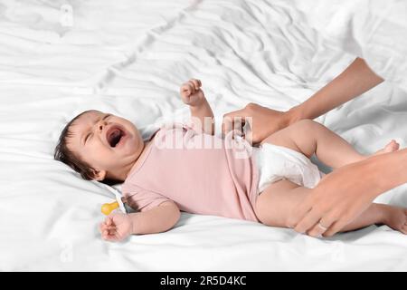 Madre che mette i vestiti sulla figlia piangente sul letto, primo piano Foto Stock