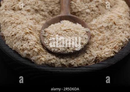 Ciotola e cucchiaio di fiocchi di lievito di birra su fondo nero, primo piano Foto Stock