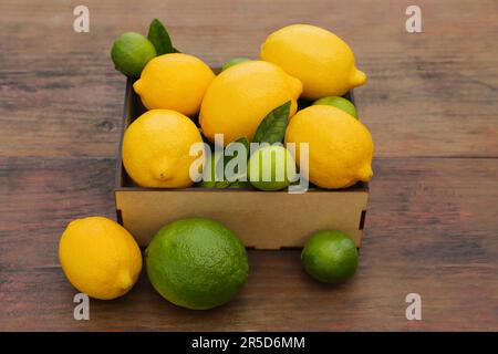 Molti limoni freschi e lime con foglie su tavola di legno Foto Stock