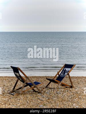 Due sedie a sdraio vuote affacciate l'una sull'altra sulla spiaggia di ghiaia deserta Foto Stock