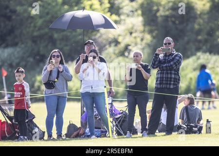 I genitori che guardano i bambini giocano alla partita di calcio di GrassRoots e girano il gioco sui telefoni cellulari nel Regno Unito Foto Stock