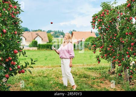 Ritratto all'aperto di felice giovane donna in campagna, modello femminile lancio di mela in aria Foto Stock