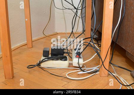 Ingombro dei cavi causato da più prolunghe elettriche e connettori maschio multi-contatto su pavimenti in legno. Cavi aggrovigliati sul pavimento in parquet. Foto Stock