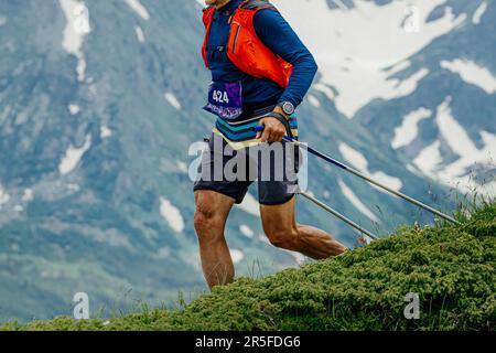 atleta che corre la maratona paracadutismo gara su prato verde in background montagna innevata, sulle spalle camelbak Foto Stock