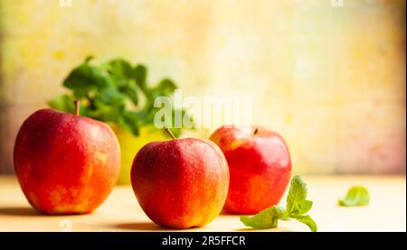 Ancora la vita con mela rossa e menta fresca in ciotola su sfondo giallo. Vista frontale, spazio di copia. Foto Stock