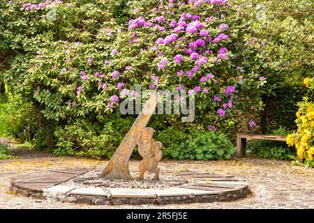 Attadale Gardens Wester Ross Scotland fiori di rododenron viola circondano l'orologio con gnomone e gatto selvatico Foto Stock